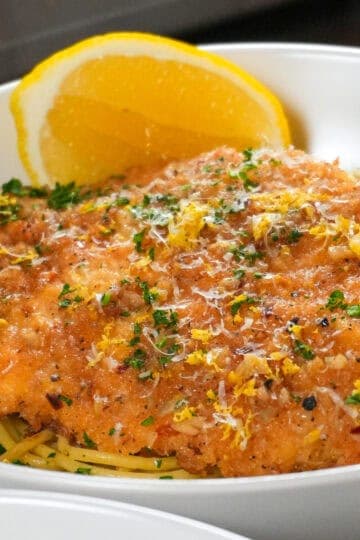 Crispy fried chicken on spaghetti with lemon and parsley garnish, a delicious poultry dish.